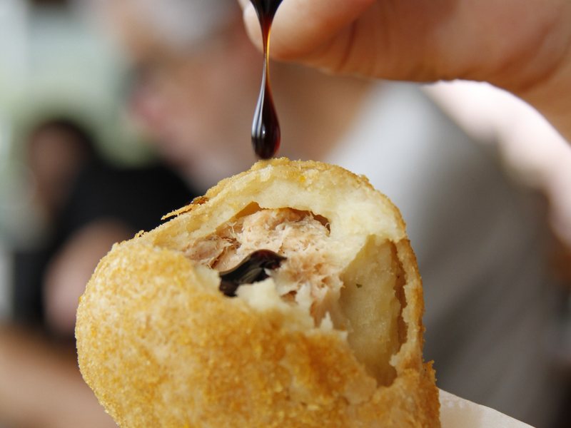 Cliente colocando molho na coxinha aberta, no salão do Kiosque Roseira
